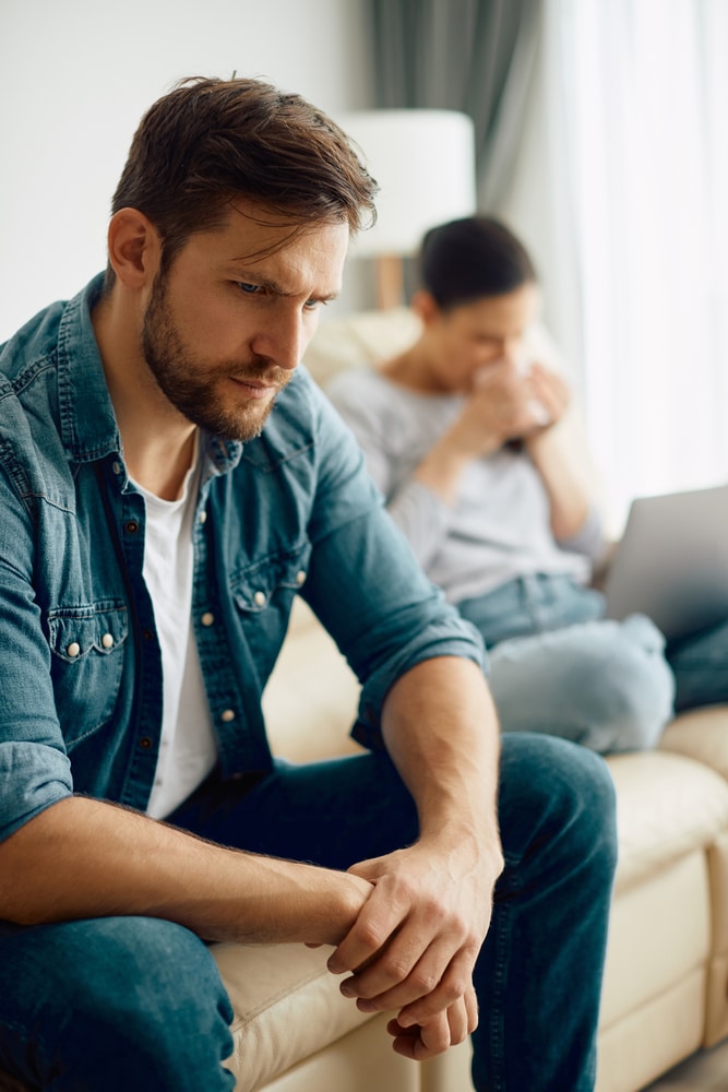 A man looks distraught while sitting next to a woman on a couch.