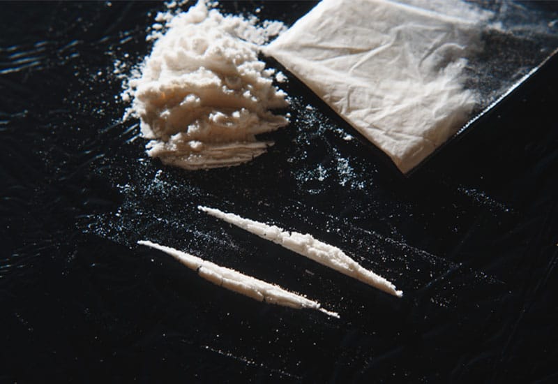 Lines of white powder, a small pile of white powder, and a baggie of white powder on a black surface