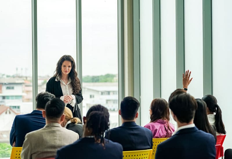 A woman standing and speaking in front of a group of people sitting in chairs.