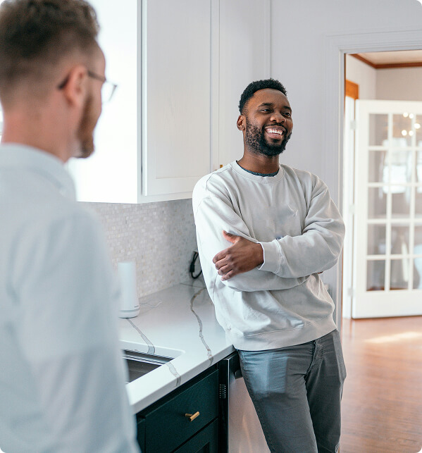 Person wearing a light gray sweatshirt leaning on a kitchen counter and smiling.