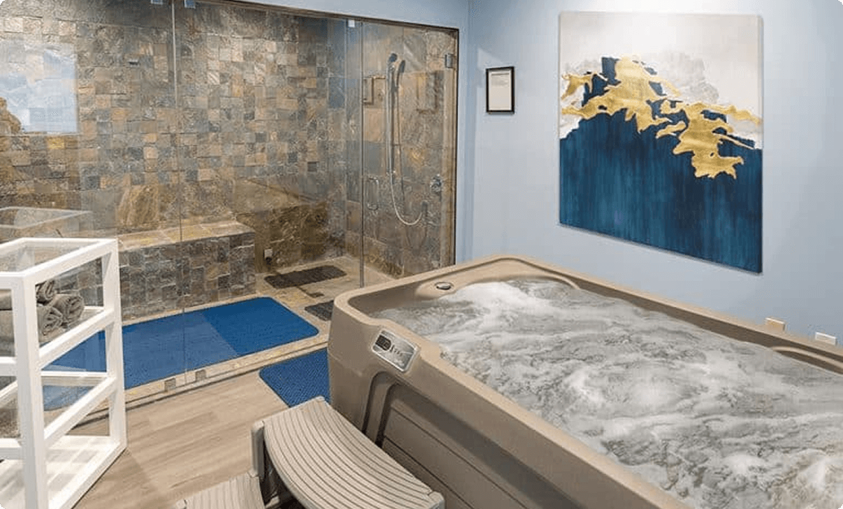 Jacuzzi in a spa room with stone tile shower and abstract painting on the wall.