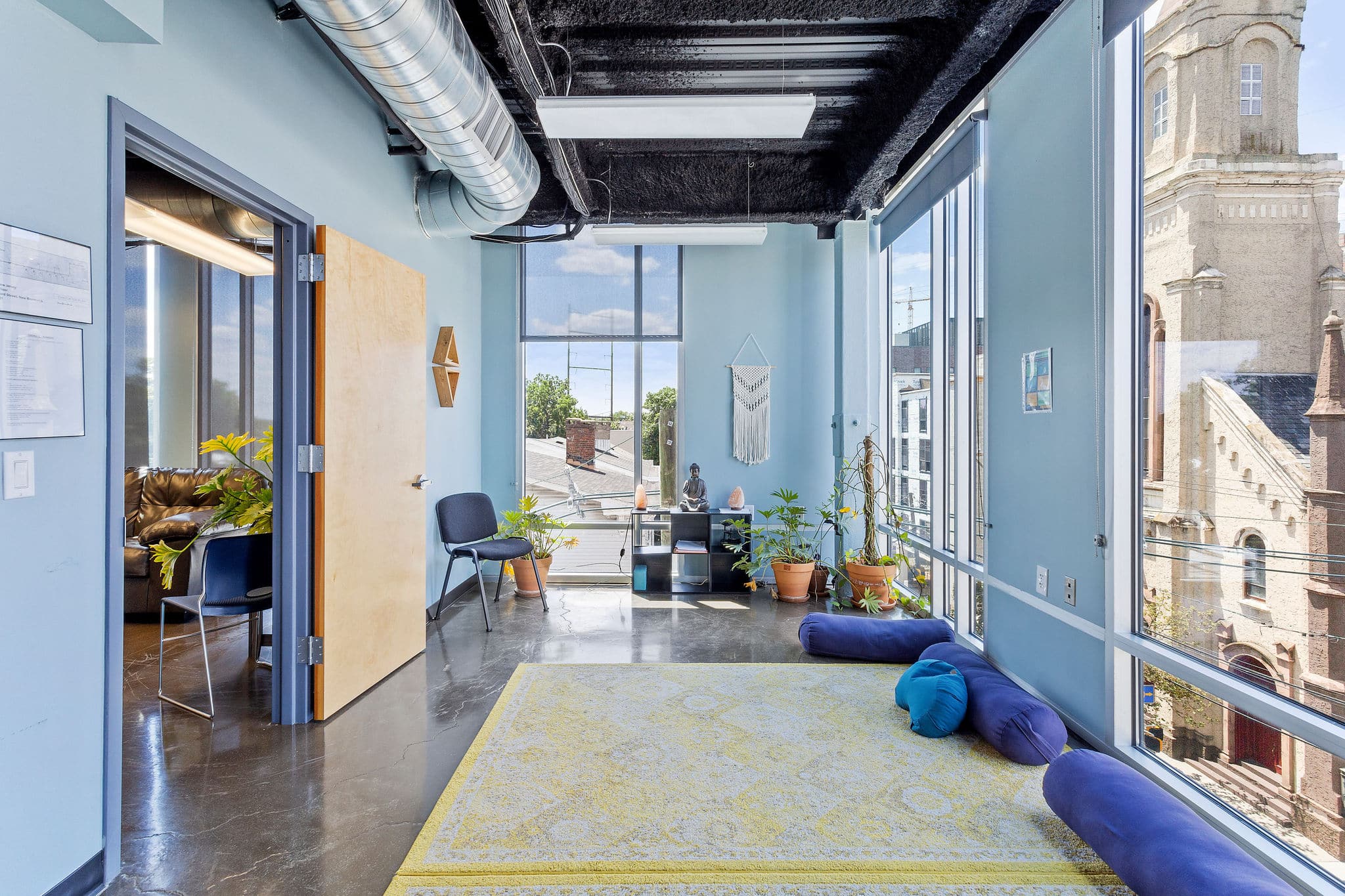 Modern office space with plants, chairs, and large windows overlooking a cityscape with a church building.