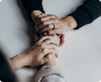 Two people holding hands, one in a dark sweater, the other in a light sweater, on a white table.