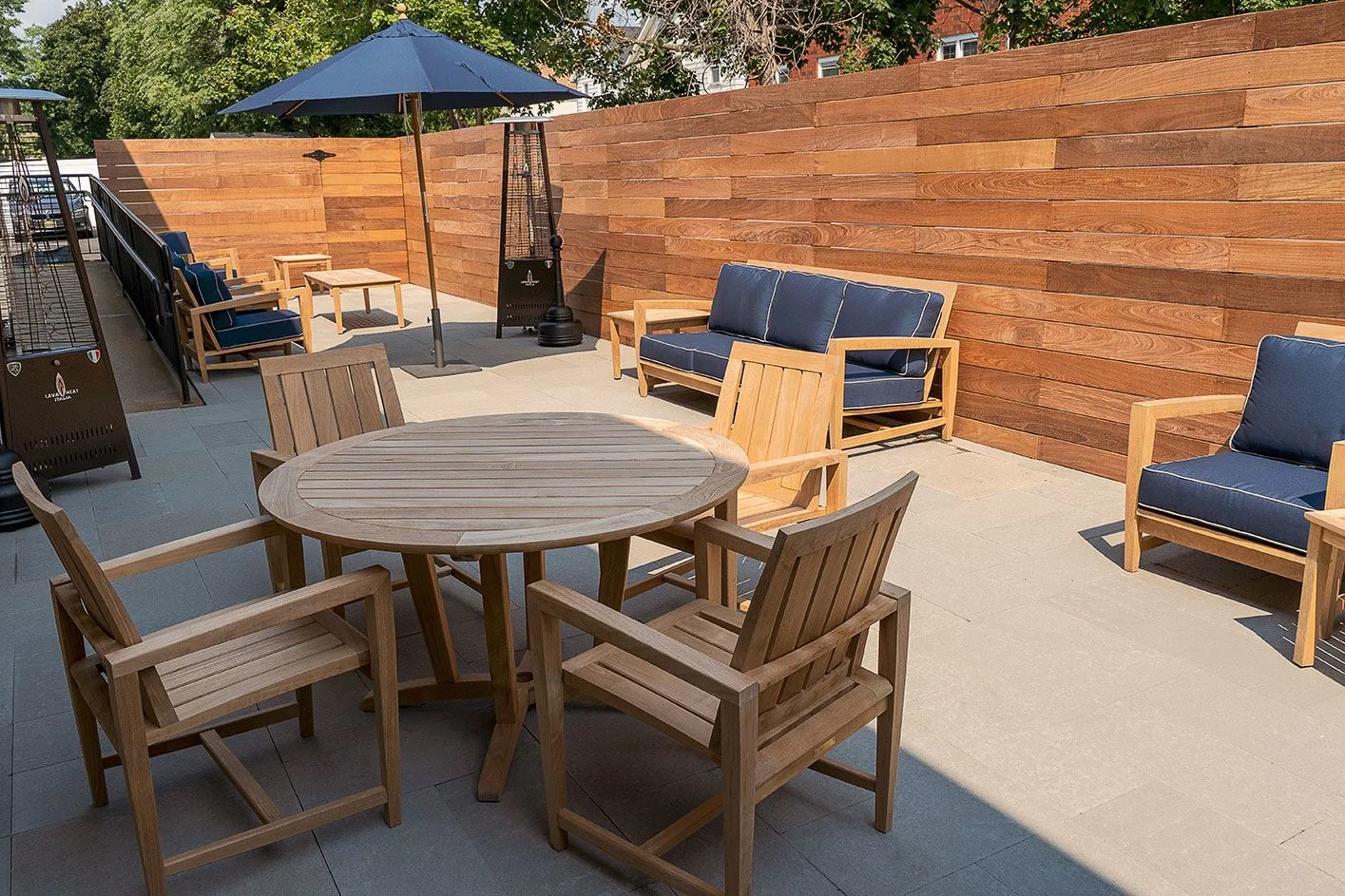Outdoor patio with wooden furniture, blue cushions, and an umbrella against a wooden fence.