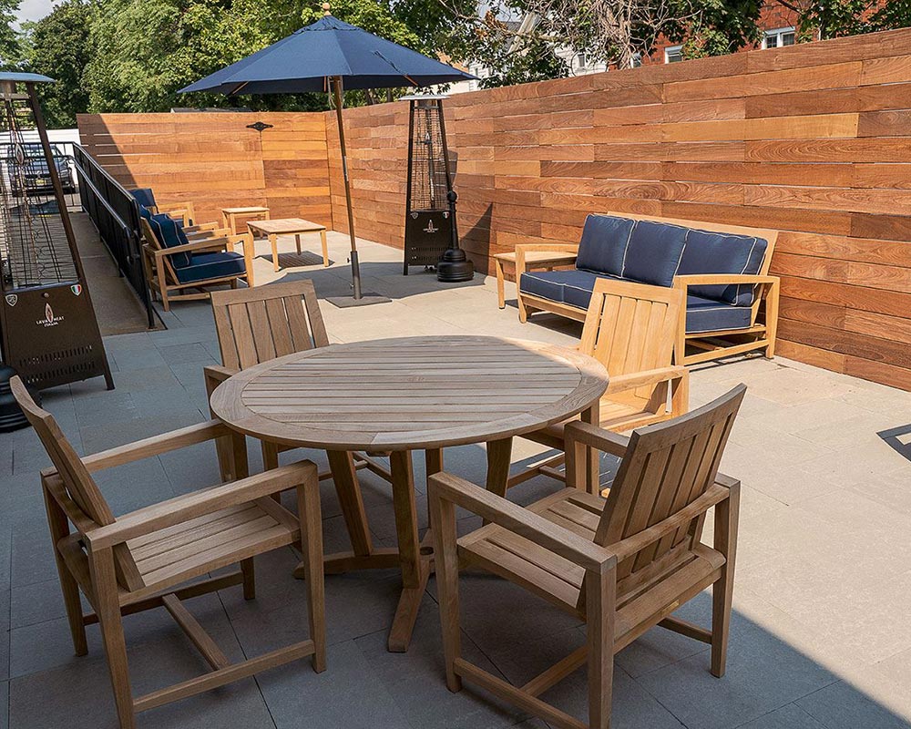 Outdoor patio with wooden furniture, blue cushions, and an umbrella against a wooden fence background.