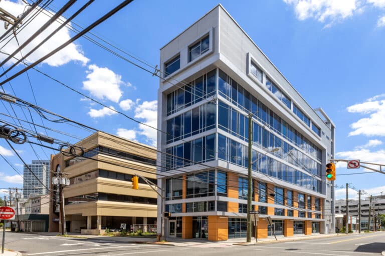 Modern glass office building on a sunny day with blue sky and clouds.