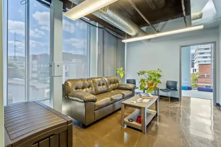 Lobby with brown leather sofa, coffee table, plants, and large windows.