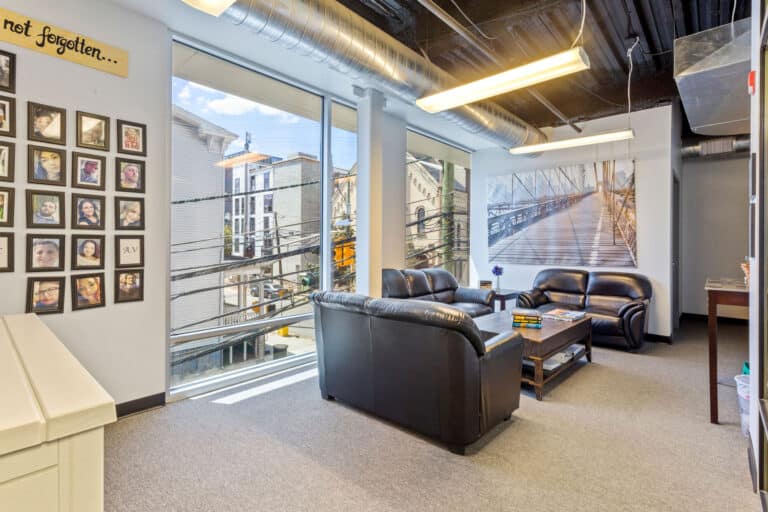 Room with leather sofas, large windows, photo wall, and city view.