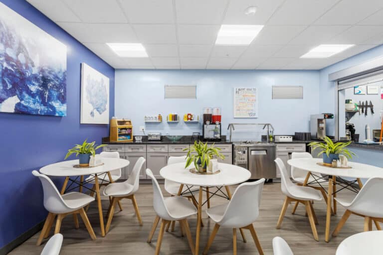 Modern kitchen area with round tables, white chairs, and vibrant blue walls.