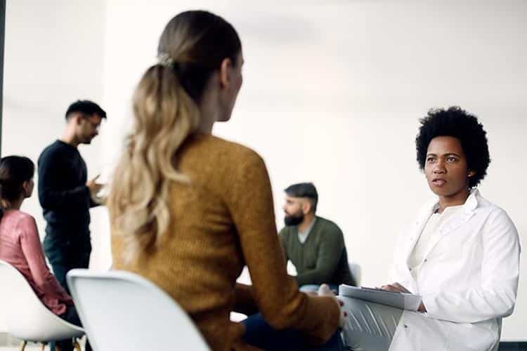 Person wearing a white coat holding a clipboard in a group meeting.