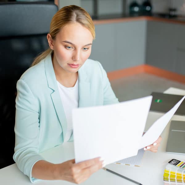 Person in light blue blazer reading documents at desk.