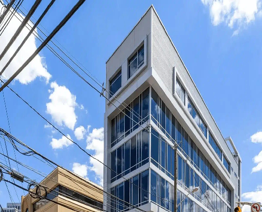Modern glass office building under a blue sky with clouds.