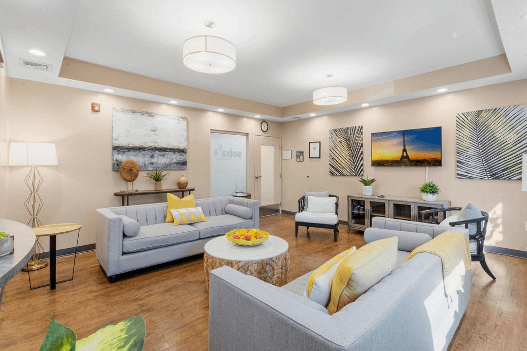Room with modern gray sofas, yellow accents, wall art, wooden floor, and warm lighting.